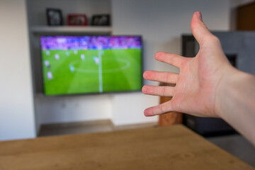 A male hand expressing frustrations towards a soccer match that is visible on the tv screen.