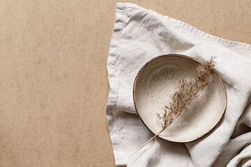 Fototapeta na wymiar Minimalist ceramic bowl with dry plant over kraft paper background. Copy space, flat lay.