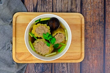 Stuffed bitter gourd with seasoned minced pork in clear soup served on wooden tray.