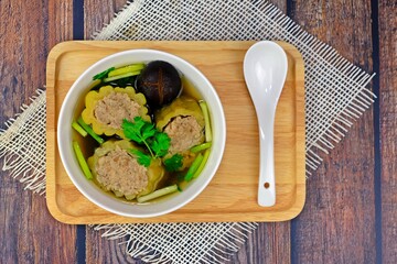 Stuffed bitter gourd with seasoned minced pork in clear soup served on wooden tray.