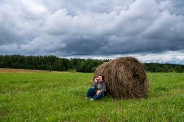 woman resting near a haystack in nature against a gray sky