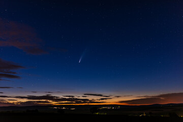 Comet Neowise C/2020 F3 in the blue sky with his tail and sunset. Landscape photo with isolated clouds and orange sunset