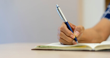 close up senior woman using pen to writing on notebook diary to planning about pension life and investment or daily activity at home for mature health and lifestyle in relax time concept