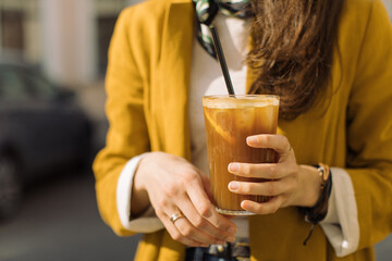 Young woman holding glass of iced coffee on summer terrace. Close up, copy space.