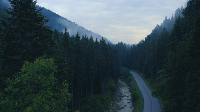 Asphalt road going through the mountains. A mountain stream flows along the road and intersects with it