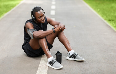Fototapeta na wymiar Sporty black guy resting and using his smartwatch