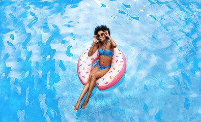 Summer time. Beautiful black woman in bikini swimming on inflatable ring at pool during tropical vacation, above view