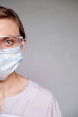 Close up of female doctor or scientist with a medical mask and glasses over grey background.