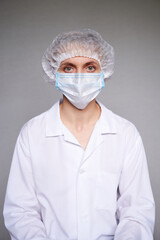 Close up of female doctor or scientist with a medical mask and surgical cap over grey background.