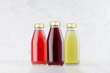 Red, pink, green fruit juices set in glass bottles with cap mock up group on white wood table in light interior, template for packaging, advertising, design product, branding.