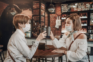 Friends girls in a cafe and communicating with each other. Drink coffee and wear medical protective...