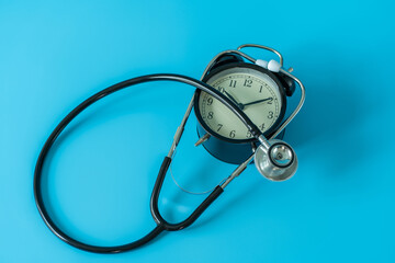 Stethoscope and vintage clock on blue background. Medical and health care concept