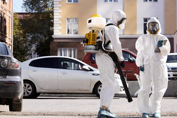 brave professional disinfectors in protective hazmat suit walking through city streets and spraying disinfectant to stop spreading highly contagious coronavirus or COVID-19, use special equipment