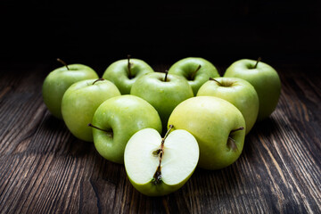 Fototapeta na wymiar several whole fresh green apples grouped in a triangle form lie on a dark wooden table with half an Apple in the foreground