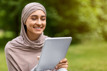 Smiling arab girl using digital tablet at public park, checking
