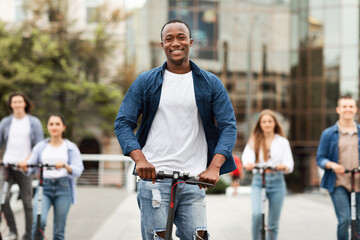 Five excited friends having ride on electric kick scooters