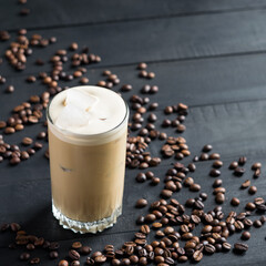 Iced coffee with milk in a tall glass on a black wooden background with coffee beans. Selective focus