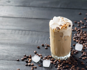 Iced coffee with milk in a tall glass on a black wooden background with coffee beans. Selective focus