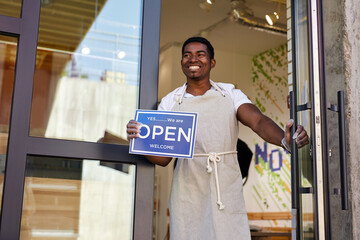 cheerful man open the door of cafe, african entrepreneur is happy to open store, invites people to...