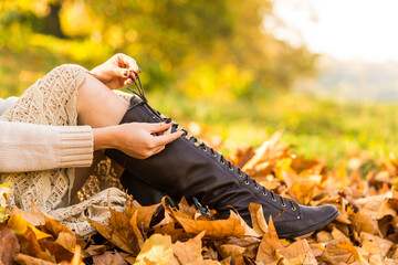 Autumn shoes. Brown boots close up in falls leaf. Woman ties shoelaces in autumn forest.
