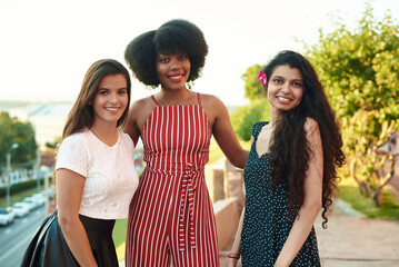 Three beautiful smiling girlfriends. Multi ethnic group of women staying outdoors by the city street and smiling