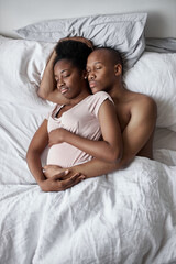 young black african couple sleeping sweetly together at home, man hugs his pregnant wife, in love