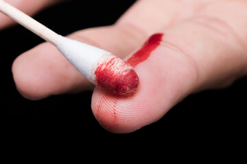 Use a cotton swab to wipe the blood at the wound on fingertips that are bleeding on dark background.