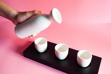 Sake rice wine flask and glass set on black and pink background