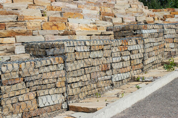 Construction of a wall in a park made of natural rough brown stone, reinforced with metal mesh.