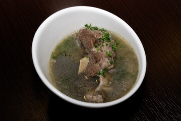 meat in the broth with some herbs served in the white bowl
