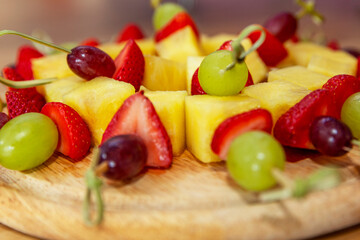 Appetizing fruit canapes of strawberry, pineapple and grapes on a wooden board. Close-up. Buffet snacks.