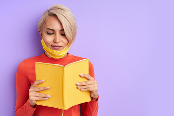 portrait of attractive young woman in mask with book in hands, people read books, immersed in learning, in enlightenment during quarantine. stay home