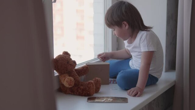 Toddler sits on windowsill and plays with scattering pills without parent's control. Dangerous situation with little boy. Medicines are freely available to child.