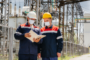 Engineers electrical substations conduct a survey of modern high-voltage equipment in the mask at the time of pandemia. Energy. Industry