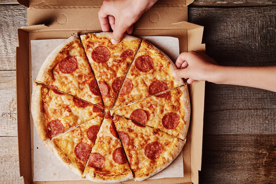 Two hands takes slices of pizza from cardboard box, top view