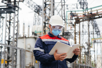 An electrical substation engineer inspects modern high-voltage equipment in a mask at the time of pondemia. Energy. Industry