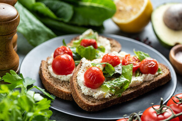 Fototapeta na wymiar Tasty sandwich with soft white ricotta cheese, roasted tomatoes and basil garnished with crushed pepper and olive oil