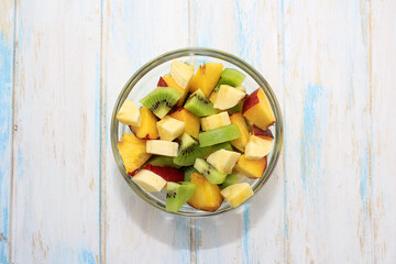 Summer fruit salad with banana, kiwi, peach in glass bowl on wodden background. Copy space