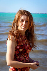 A serious young woman on the beach with gorgeous red hair and freckles.