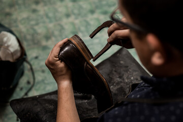 Male cobbler sitting at his shop and repairing man's shoe made of brown leather.