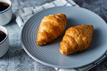 Fresh croissants on a plate with cups of coffee