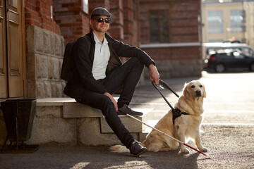 young sick man with helpful guide dog in city streets, sit having rest, man and golden retriever,...