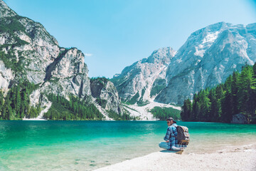 man sitting on the beach of the lake with backpack mountains in background