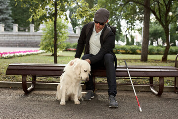 young blind man stroke his helpful dog guide, kind golden retriever love his owner, while walking outdoors