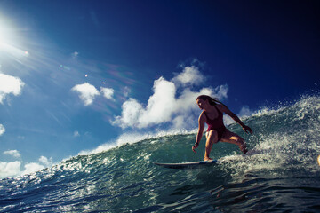 Professional Surfer Girl riding wave on surfing board under bright sun on background. - obrazy, fototapety, plakaty