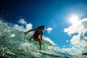 Professional Surfer Girl riding wave on surfing board under bright sun on background. - obrazy, fototapety, plakaty