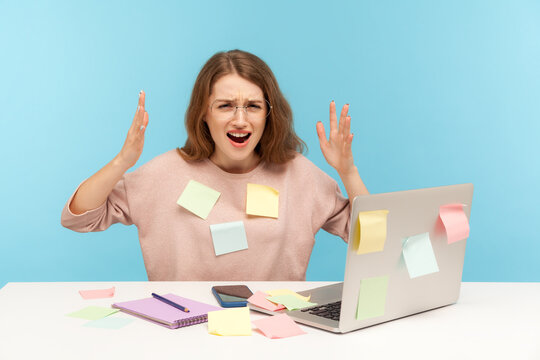 Stressful job. Depressed overworked woman employee in glasses covered with sticky notes, angrily raising hands, screaming in desperate, loaded with work. indoor studio shot isolated on blue background