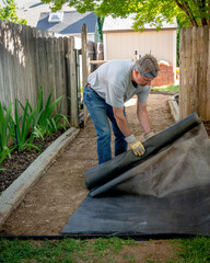 yard worker man lays down landscaping fabric on the ground