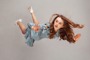 Beautiful girl levitating in mid-air, falling down and her hair messed up soaring from wind, model...