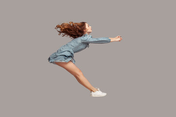 Side view girl rushing at full speed accelerate, steering driving fast and levitating in air. Model flying rapidly with hurricane wind blowing extremely sharply. indoor studio shot isolated on gray